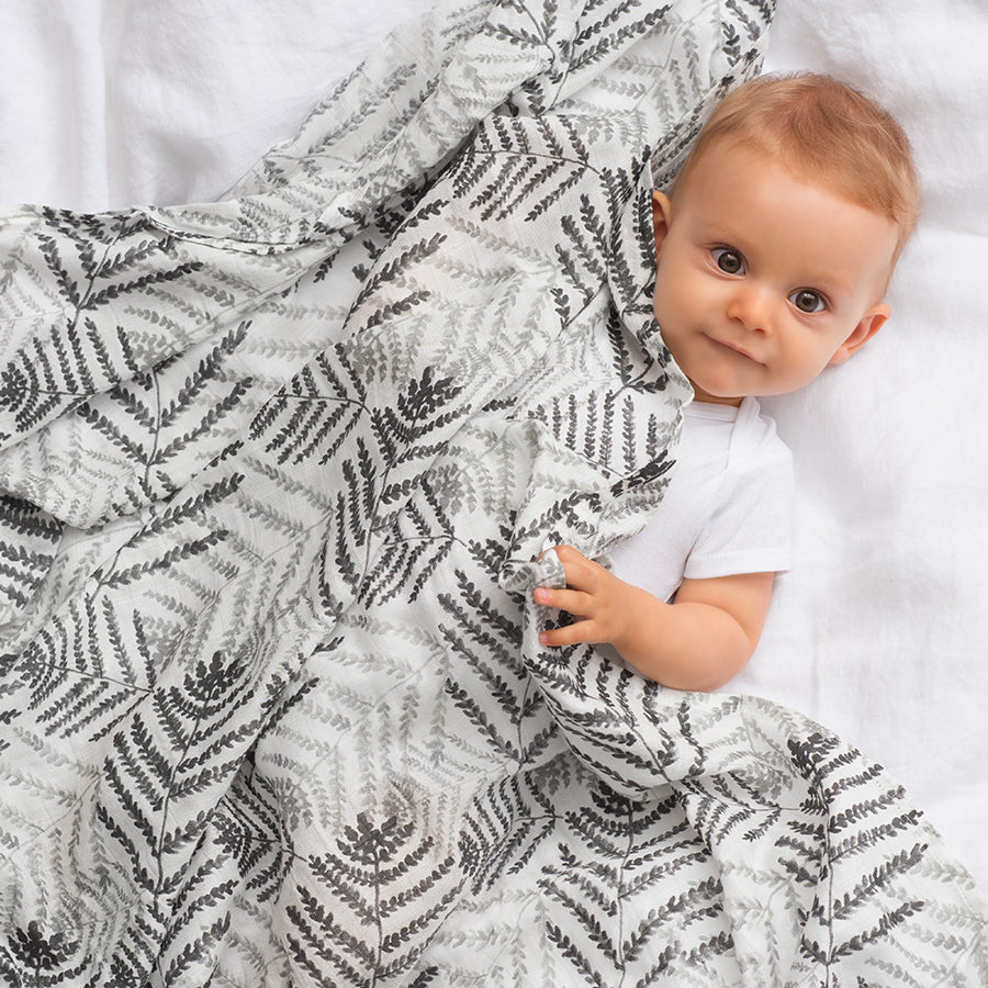 baby boy covered with gray muslin swaddle 